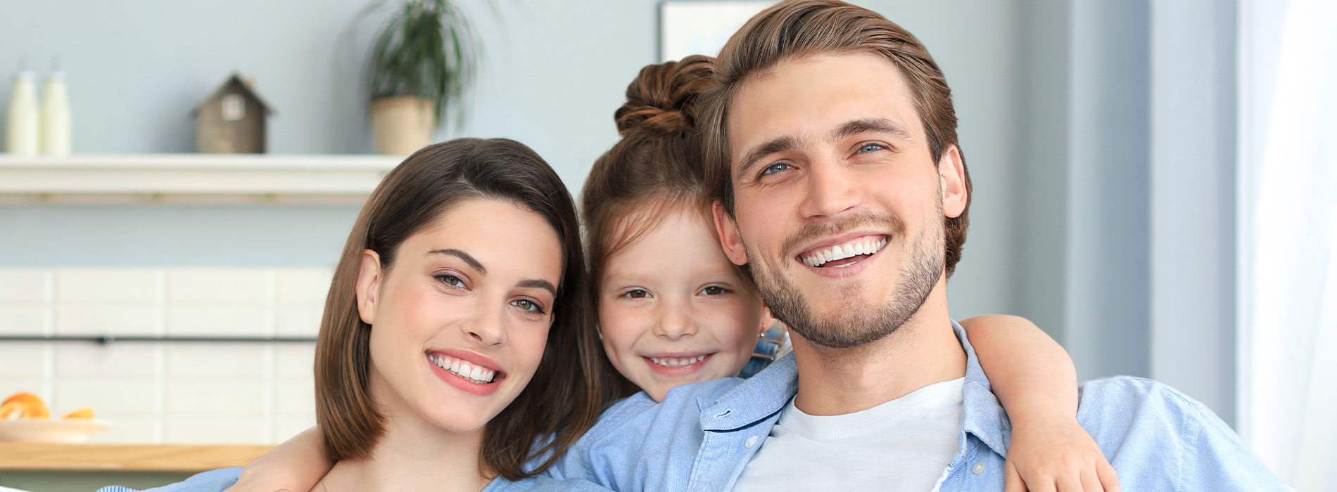 A family of four, a man, a woman, and two children, smiling in front of a kitchen counter.