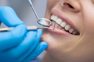 The image features a woman receiving dental care, with a dental hygienist using a mirror and dental tools to clean her teeth.