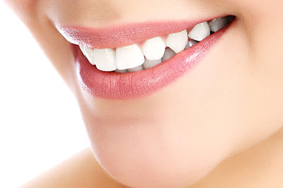 The image shows a close-up of a person s face with a focus on their smile, featuring white teeth and pink lips.