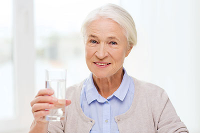 An elderly woman in a blue cardigan holding a glass of water.