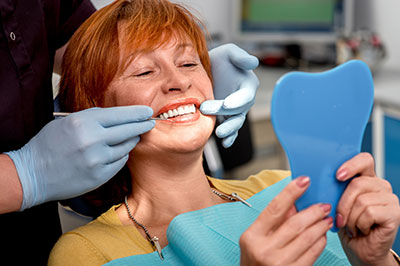 The image shows a person with red hair sitting in a dental chair, wearing a blue mask and holding a toothbrush, while another individual is adjusting their teeth.