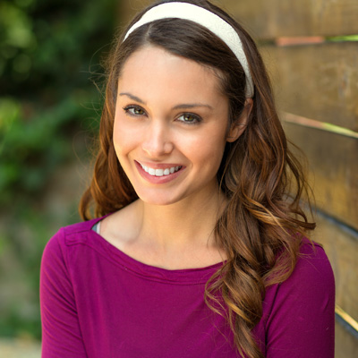 A woman with long hair, wearing a purple top and a headband, smiling at the camera.