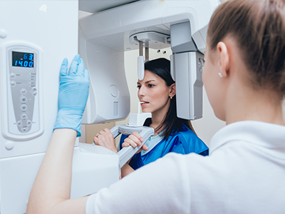 A woman in a blue jacket is standing next to a large, white CT scan machine.