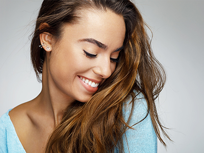 A smiling young woman with long hair, wearing a light blue top, stands against a neutral background.