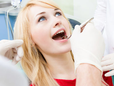 A woman is seated in a dental chair, receiving dental care from a professional, with a smile on her face.