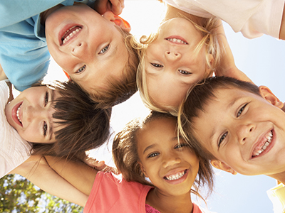 The image is a group photo of six children, three boys and three girls, smiling at the camera with their arms around each other.