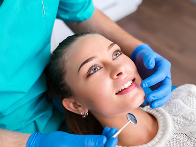 A dental professional performing a procedure on a patient s teeth, with the patient smiling and looking upwards.