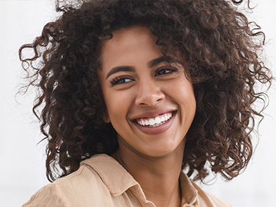 A smiling woman with curly hair, wearing a brown top, against a white background.